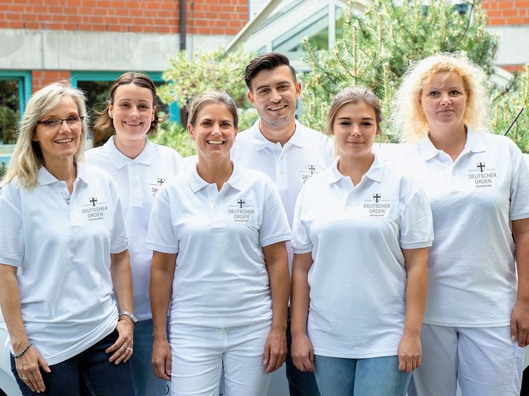 Gruppenfoto: Pfleger/innen in weissen DO-Shirts vor einem weissem Kleinwagen